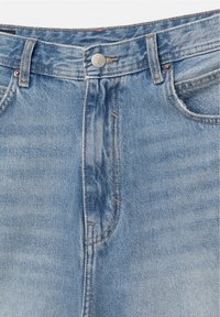 Jean en denim bleu clair en gros plan montrant la taille, la fermeture à bouton, les passants de ceinture, les poches avant et les coutures détaillées.
