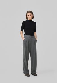 T-shirt en col roulé noir à manches courtes associé à un pantalon gris large à taille haute, avec fermeture à bouton et poches latérales.