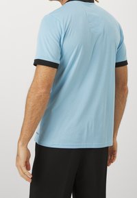 Ljusblå idrottströja med ribbad textur, svarta krage- och ärmdekorationer. Korta ärmar, rundad nederkant och enkelt design.