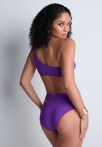 Ensemble de bikini violet avec un haut à une épaule et un bas taille haute, présentant une texture lisse et des accents dorés subtils.