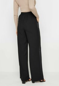 Pantalons larges noirs en tissu léger avec une taille élastique et des panneaux en satin sur les côtés. Texture lisse avec une coupe décontractée.