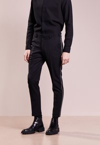 Svarta figurnära byxor med vita sidosträck, tillverkade av ett slätt material. Matchas med en svart långärmad tröja och svarta chelsea-boots.