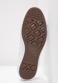 Semelle d'une chaussure Converse All Star blanche montrant une bande de roulement en caoutchouc brun avec des motifs géométriques et le nom de la marque embossé.