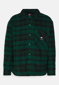 Camicia a quadri verdi e neri realizzata in tessuto morbido; presenta una chiusura con bottoni, colletto e una tasca con etichetta del logo sul petto.