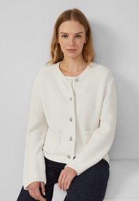 Cardigan blanc en tricot avec des manches longues, un col rond, des boutons en métal argenté et des poches frontales. Tissu texturé et poignets côtelés.