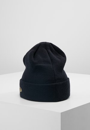 Bonnet noir en tricot avec revers plié et petit logo brodé en or, présenté sur une surface blanche contre un fond uni.