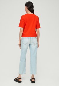 Rode korte mouwen t-shirt gecombineerd met lichtblauwe rechte jeans. Zwarte sandalen maken de casual outfit compleet. De achterkant laat een eenvoudig ontwerp zien.