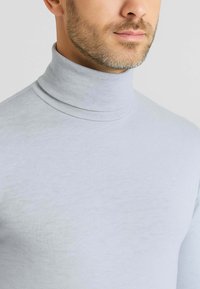 Maglione a dolce vita grigio chiaro realizzato in tessuto morbido, con un design aderente e colletto alto. Texture liscia con cuciture sottili.