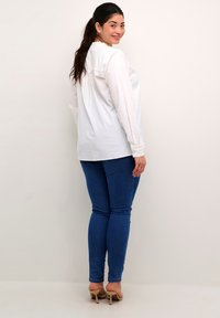 Hvid langærmet bluse med rund halsudskæring, parret med blå skinny jeans og beige højhælede sandaletter. Glat stof og tætsiddende design.