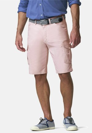 Man draagt lichtroze cargoshort, een gevlochten riem, een blauw overhemd met knopen en blauwe sneakers, staand tegen een witte achtergrond.