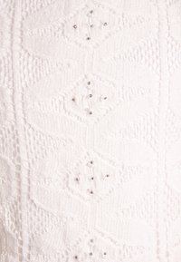 Biały dzianinowy wyrób z teksturowanymi wzorami i małymi metalowymi koralikami równomiernie rozmieszczonymi w całym projekcie, zwiększającymi detal wizualny.