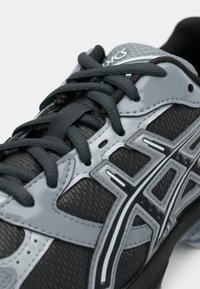 Juodas sportinis batelis su pilkomis detalėmis, turintis tekstūruotą viršutinę dalį, raištelius ir atspindinčius akcentus. Sukurtas palaikymui ir ilgaamžiškumui.