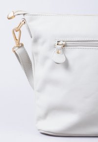 White leather shoulder bag with a zip closure, flat front, adjustable strap, and a small exterior zip pocket with gold hardware accents.