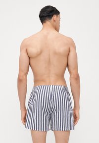 Maillots de bain rayés en bleu marine et blanc, dotés d'une taille élastique et d'une coupe ample, avec une texture lisse semblable au coton.
