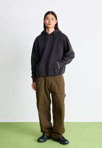 Sort bomulds-hættetrøje med en frontlomme, parret med olivengrønne cargo-bukser med sidelommer og en løs pasform. Sorte sneakers fuldender looket.
