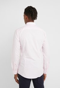 Camicia a maniche lunghe rosa chiaro con colletto a punta, texture liscia e design aderente. Presenta polsini con bottoni e orlo curvo.