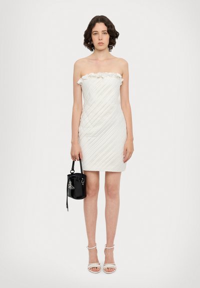 Strapless witte jurk met een ruches Halslijn en diagonale plooien. Combinatie met een kleine zwarte handtas en witte sleehakken.