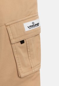 Beige tkaninová kapsa na cargo s klopou a černou tabulkou, s bílým štítkem značky Vingino s nápisem "Pro lásku k denimu".