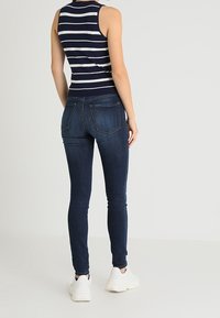 Top sin mangas a rayas en navy y blanco combinado con jeans skinny azul oscuro. Zapatillas blancas complementan el atuendo. Enfoque en estilo casual.