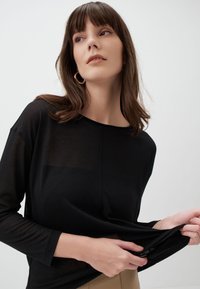Zwarte lange mouwen top met een losse pasvorm, gemaakt van een transparante, lichtgewicht stof. Heeft een ronde halslijn en subtiele stiksels.