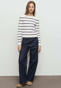 Lange mouwen, off-white shirt met marineblauwe horizontale strepen, gecombineerd met donkerblauwe broek met brede pijpen en beige schoeisel. Eenvoudige, casual look.
