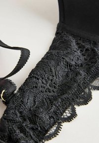 Crni čipkasti grudnjak s složenim cvjetnim uzorcima, glatkom tkaninom, podesivim trakama i valovitim rubom. Bogata tekstura s dekorativnim detaljima.
