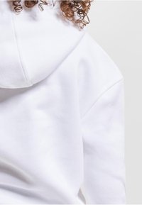 Sweat à capuche blanc avec un tissu texturé et une poche kangourou. Comprend une capuche et des détails de coutures visibles. Design doux et décontracté.