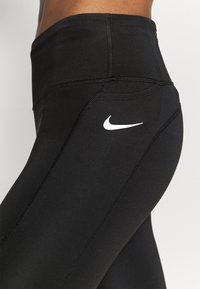 Musta korkeavyötäröinen trikoo joustavasta kankaasta, jossa on litteät saumat ja pieni valkoinen Nike-logo sivussa.