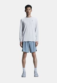 Hvid langærmet træningsskjorte med logo, parret med lyseblå shorts og grå løbesko. Glat stof, afslappet pasform, ingen mønstre.