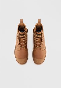 Botas de tobillo de cuero marrón con punteras redondeadas, cordones y una textura suave. Presentan una lengüeta con un tirador y el logo de la marca.