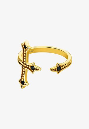 Anillo en tono dorado con diseño de cruz y extremos puntiagudos, adornado con piedras negras y detalles punteados a lo largo de la banda.