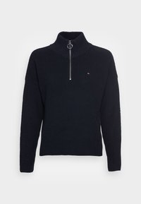 Pull-over en maille côtelée noire avec col haut et demi-fermeture éclair. Présente un petit logo sur la poitrine et des manches texturées.