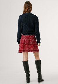 Maglione lavorato a maglia blu navy con un motivo testurizzato, abbinato a una mini gonna rossa a fantasia e stivali neri fino al ginocchio.