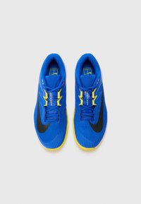 Chaussures de sport bleues avec une tige en tissu texturé, des accents noirs et une semelle extérieure jaune vif. Dotées d'un design à lacets et d'une marque bien visible.