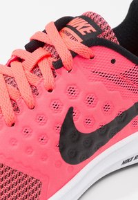 Baskets de course Nike avec un dessus texturé rose vif, un swoosh noir et des accents noirs. Elles possèdent des zones en mesh et des lacets brillants pour la ventilation.