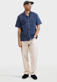 Short-sleeve button-up shirt in dark blue with a textured pattern. Paired with light beige trousers and black shoes, creating a relaxed fit.
