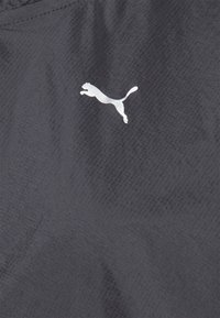 Un tissu gris foncé avec une légère texture arbore un logo Puma blanc. Le design est minimaliste, sans motifs ni embellissements supplémentaires.