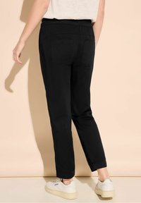 Svarta, avslappnade byxor i bomull med midjeband och två bakfickor. Uppvikta vid anklarna, tillsammans med vita skor.