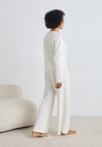 Conjunto de roupa de casa em duas peças na cor off-white, com mangas compridas e calças largas, feito de um tecido macio e texturizado com aberturas laterais.