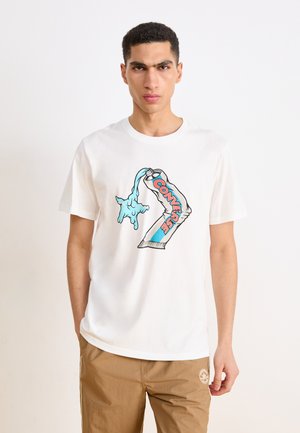 Weißes Baumwoll-T-Shirt mit einem bunten Grafikelement, das eine Hand zeigt, die blauen Flüssigkeit ausschüttet, mit dem Wort "Converse" in Rot und Blau.
