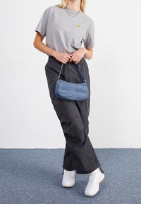 Gray short-sleeve t-shirt with a small yellow logo, black cargo pants, and a blue denim-like purse; model wears white sneakers.