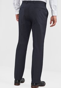Marineblauwe broek met een getailleerde pasvorm, vlakke voorkant en twee achterzakken met knoopsluitingen. De stof lijkt glad en gestructureerd.