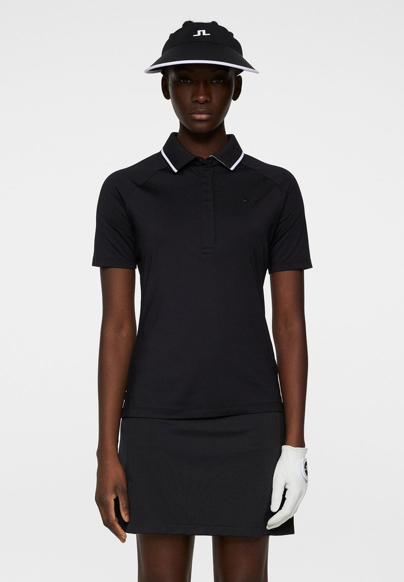 Svart polo t-shirt med korta ärmar och en vit accentkrage, kombinerad med en svart kjol, golfhandske och en visir. Slim-fit design.