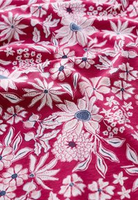 Różowy materiał z misternymi kwiatowymi wzorami w bieli i granacie, obejmującymi różne kształty kwiatów i liści, o fakturowanym wyglądzie.