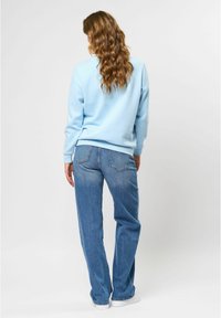 Ljusblå sweatshirt med en avslappnad passform och ribbade ärmslut, kombinerad med högmidjade blå jeans. Synliga detaljer på bakfickorna.