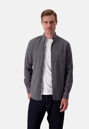 Chemise à boutons grise en tissu texturé, avec une poche poitrine et des boutons blancs, portée sur un t-shirt blanc.