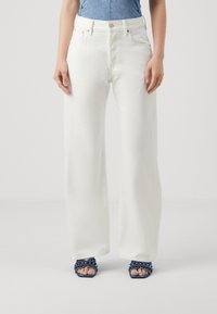 Jeans anchos blancos con cintura alta, cinco bolsillos y una textura suave. Combinados con tacones navy decorados.