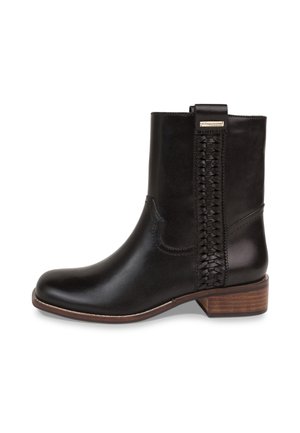 Bottine en cuir noir avec petit talon en bois, détail décoratif tressé sur le côté et petite étiquette métallique avec logo près du bord supérieur.