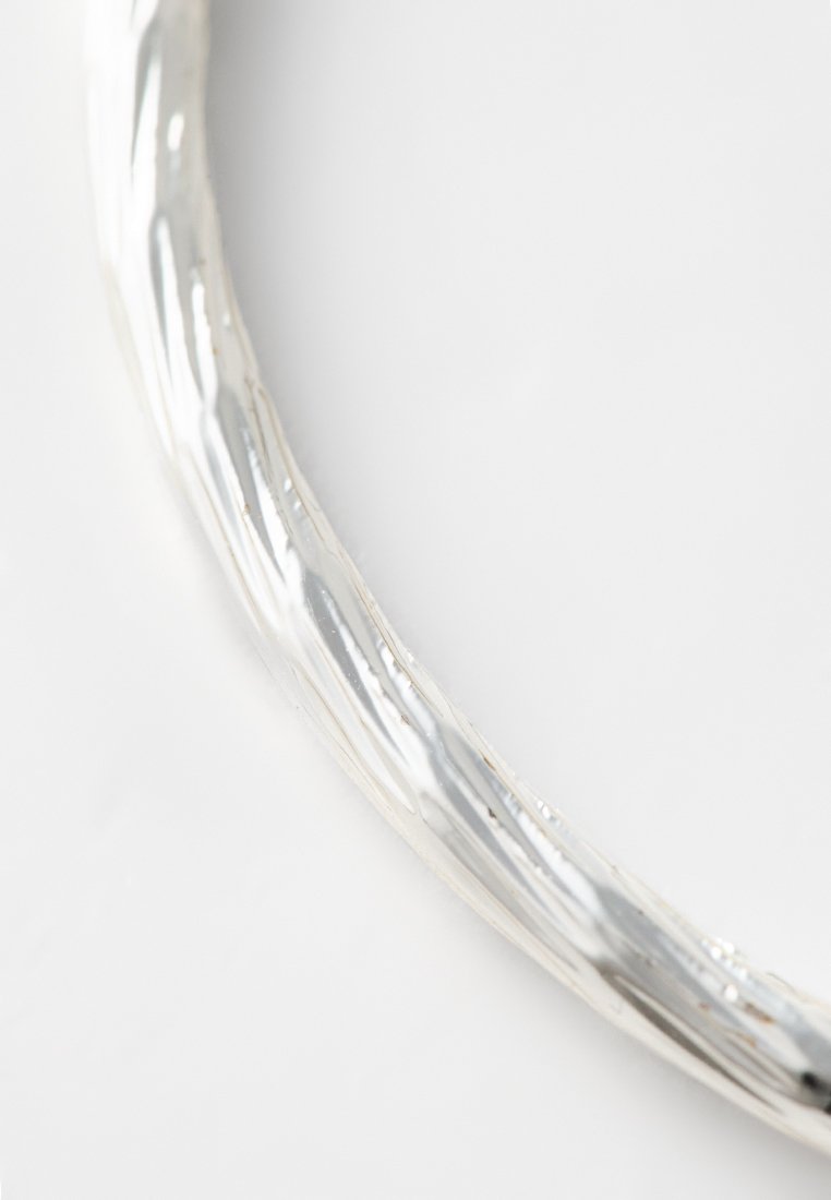 Pulsera de plata con un diseño trenzado, que presenta una superficie pulida que refleja la luz, creando una sutil textura y profundidad.