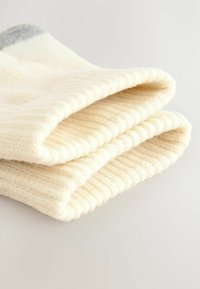 Calzini color crema, accoglienti, impilati insieme, con una texture a coste e una finitura in morbido filato. Sottili accenti grigi vicino alla cima.